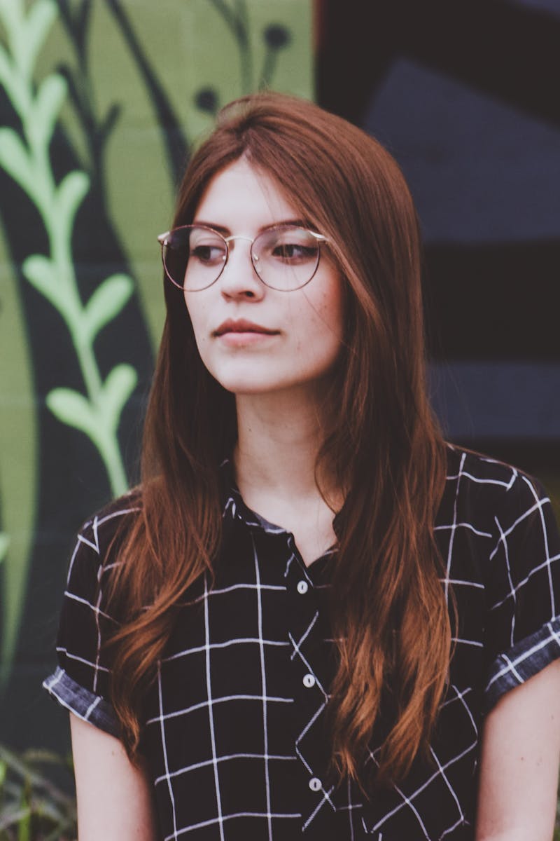 Portrait of a young woman in glasses standing outdoors against a mural background.